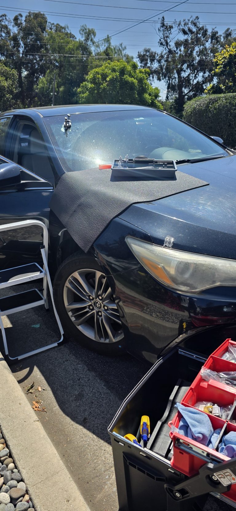 Mobile windshield chip repair in progress on a dark sedan in a driveway